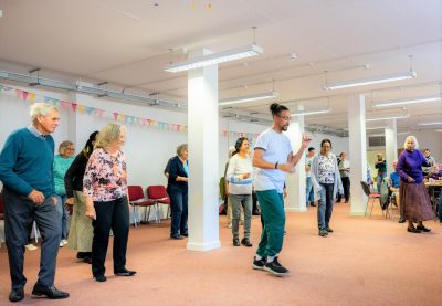 a group of older people learn dance sets from a younger man.
